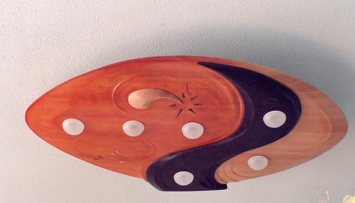 Drewniana rzeźba plenerowa w kształcie oka, z elementami w kolorze pomarańczowym, czarnym i naturalnego drewna, zdobiona rzeźbieniami i białymi, okrągłymi elementami.